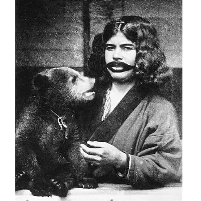 An Ainu woman with facial tattoos and a captured bear cub